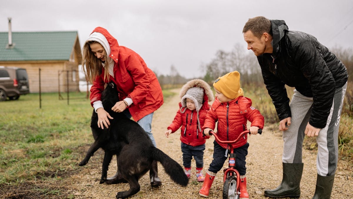 A family bonding outdoors with children playing and a pet dog in the countryside.