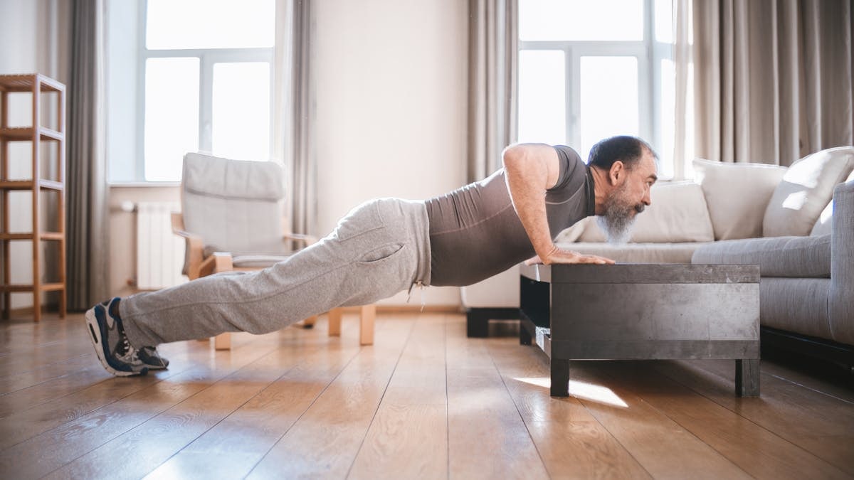 Senior man exercising at home with push-ups on a wooden floor, promoting healthy lifestyle.