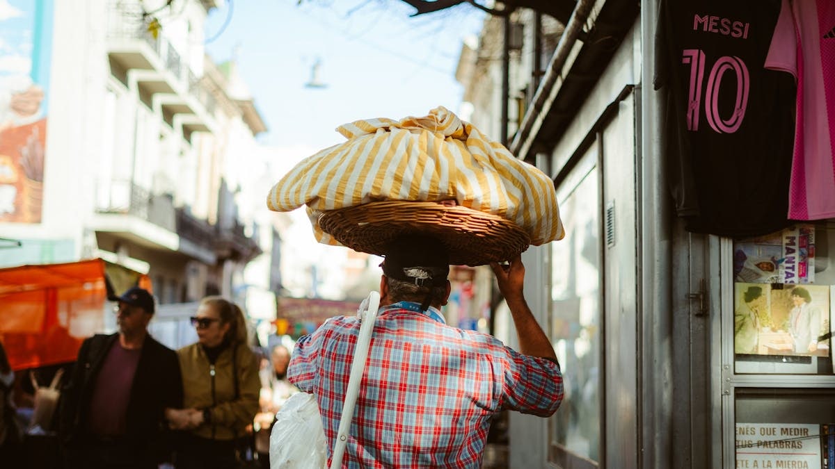 A bustling Buenos Aires street vendor carries goods through a lively market scene.